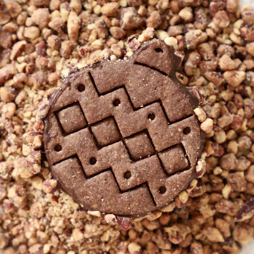 Biscuit brun en forme de boule de Noël avec un motif géométrique et des éclats sur le pourtour.