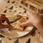 Mains séparant un biscuit étoile décoré sur une assiette, avec un petit maillet en bois.