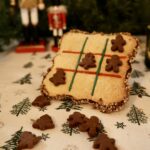 Grand biscuit décoré en jeu de morpion avec des lignes rouges et vertes et des pions sapins et bonshommes.