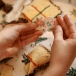Mains tenant deux disques illustrés de motifs de Noël au-dessus des morceaux d’un biscuit morpion.