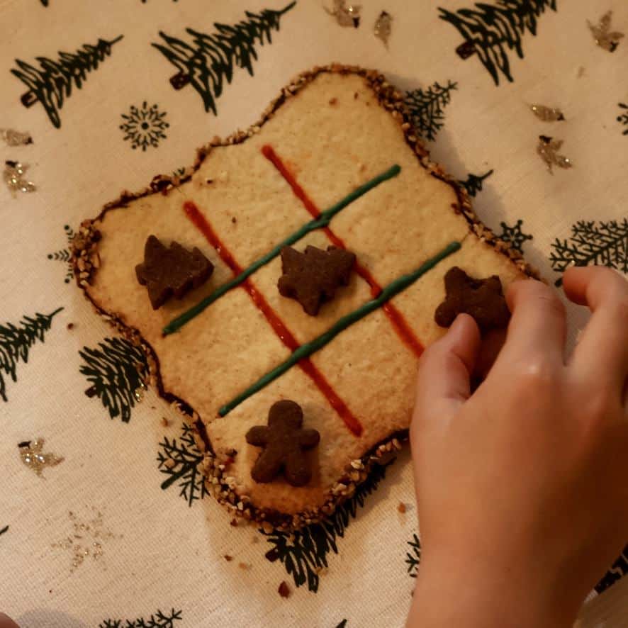 Main déplaçant un pion sur un grand biscuit jeu de morpion décoré de lignes rouges et vertes.