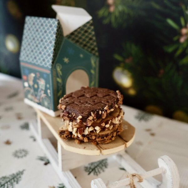 Pile de biscuits de Noël devant une boîte maison verte ouverte, sur une petite luge.