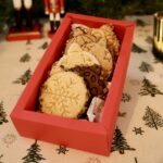 Coffret rouge ouvert avec une rangée de biscuits boules de Noël, dont un biscuit flocon au premier plan.