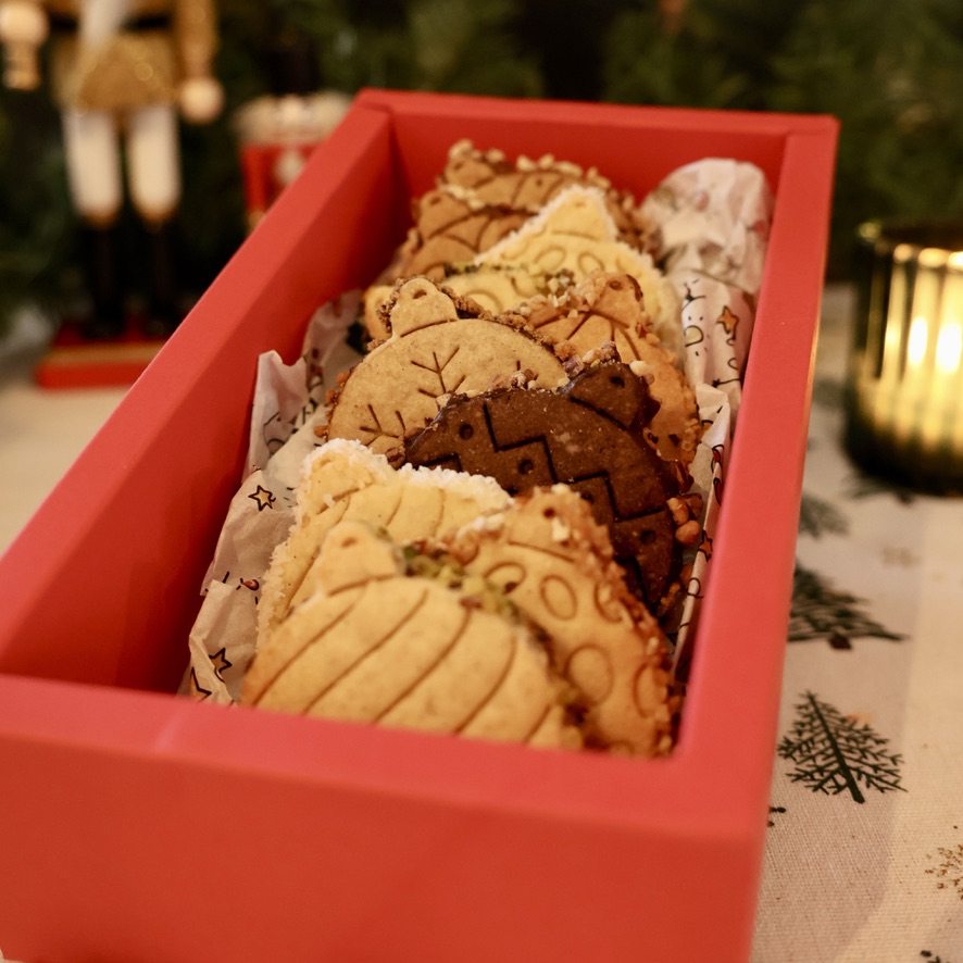 Coffret rouge ouvert contenant un assortiment de biscuits en forme de boules de Noël.