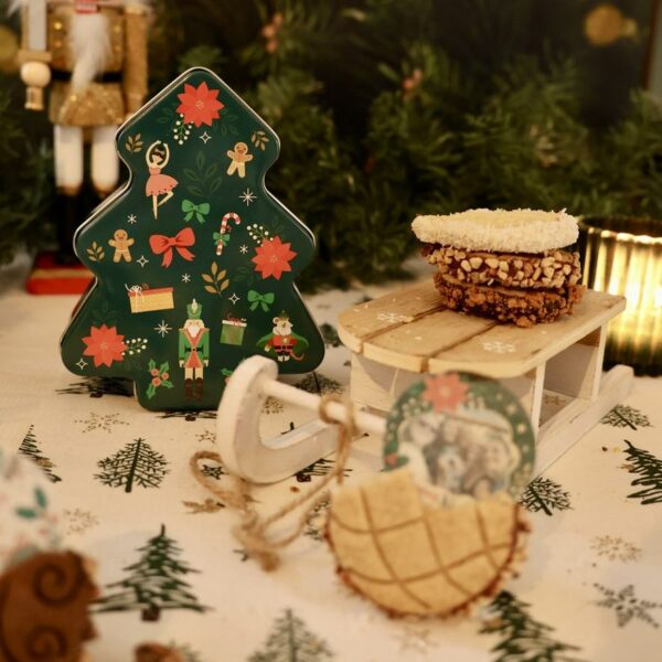 Boîte verte en forme de sapin décoré, accompagnée de biscuits présentés sur une luge.